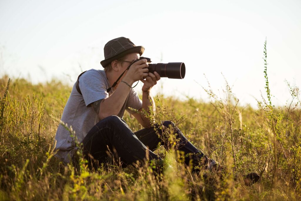 A man sits in the grass and takes pictures